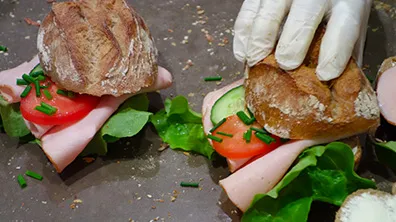 Zwei frische Sandwiches werden mit knusprigem Brot, Salat, Tomate, Gurke, Schinken und gehacktem Schnittlauch auf einer Arbeitsfläche zubereitet.