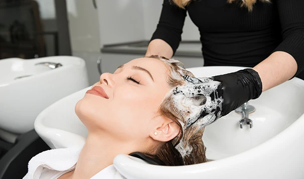 Friseur wäscht die Haare eines Kunden am Waschbecken im Salon mit schwarzen Handschuhen und schäumendem Shampoo.