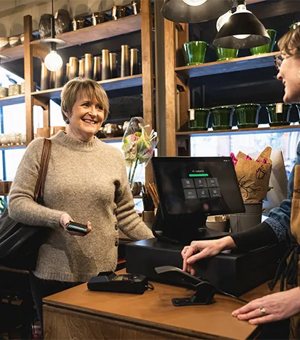 Kunde an einer Ladentheke hält ein Smartphone für kontaktlose Zahlung in der Nähe eines modernen Kassenterminals.