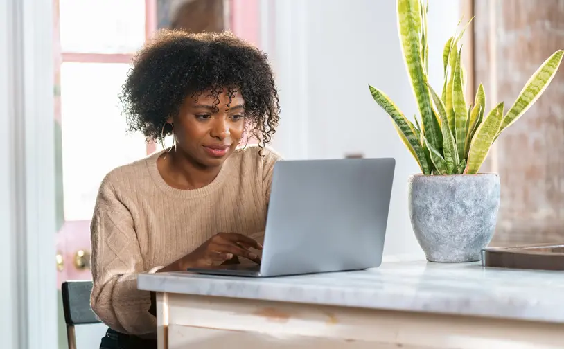 Person nutzt einen laptop an einer küchentheke mit einer topfpflanze im hintergrund