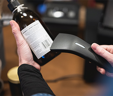 Nahaufnahme von händen die einen barcode auf einer flasche mit einem handscanner scannen