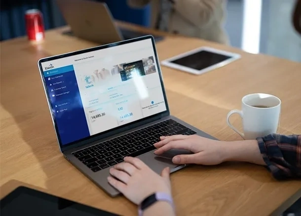 Person nutzt laptop für online banking an holztisch mit tasse und tablet