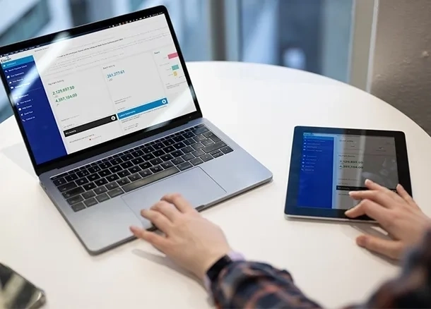 Person nutzt laptop und tablet an weißem tisch mit finanzdaten und diagrammen auf den bildschirmen